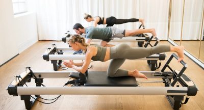 Group of friends doing pilates kneeling glutes exercises on reformer beds in a gym in a health and fitness concept