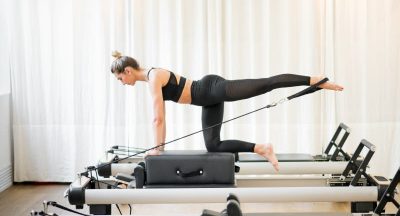 Woman performing a pilates diagonal stabilisation exercise using a strap on a reformer bed in a gym in a health and fitness concept